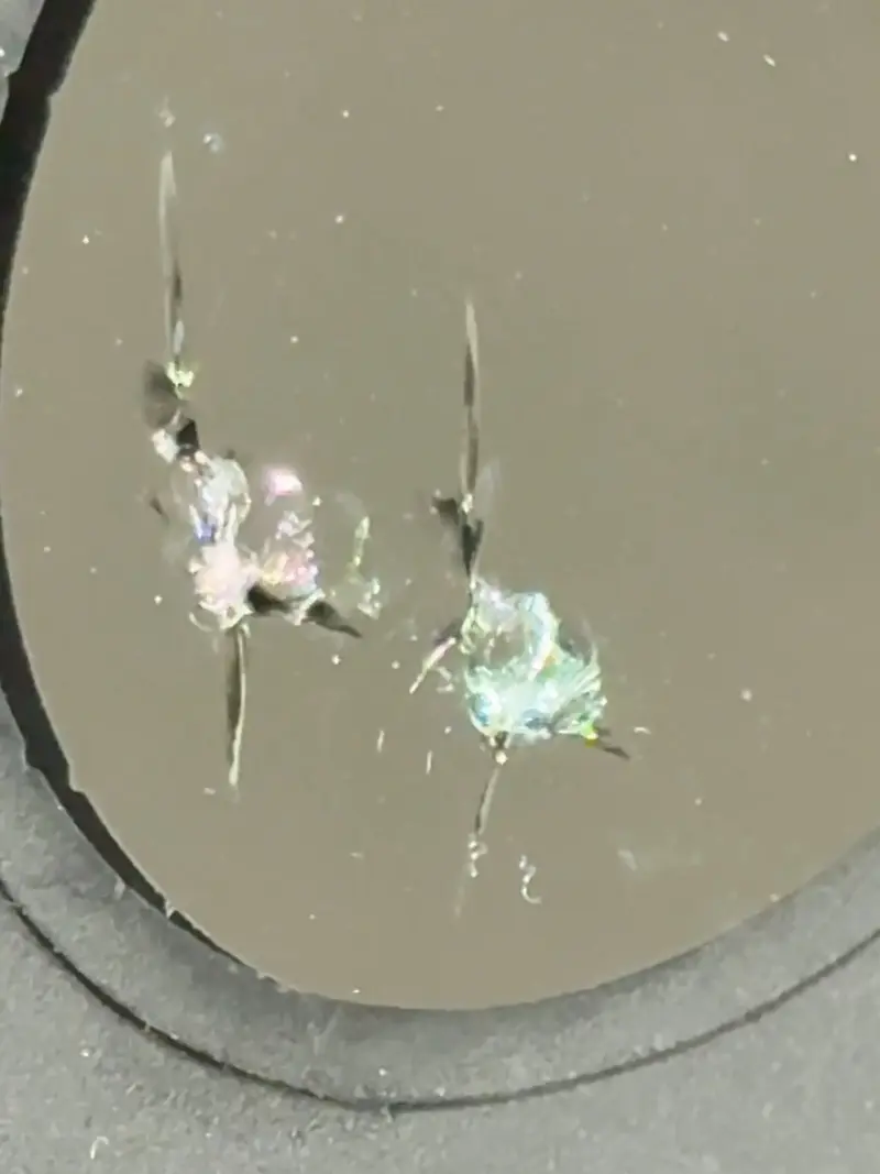 Windshield rock chip before repair viewed through inspection mirror.