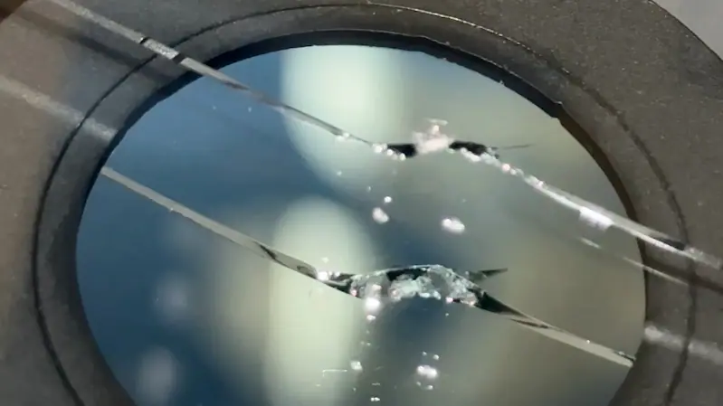 Windshield crack before repair viewed through inspection mirror.